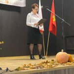 Zdjęcie przestawia uczestniczkę konkursu, która stoi na scenie i recytuje wiersz, na scenie widać również jesienną dekorację z liści i dyni